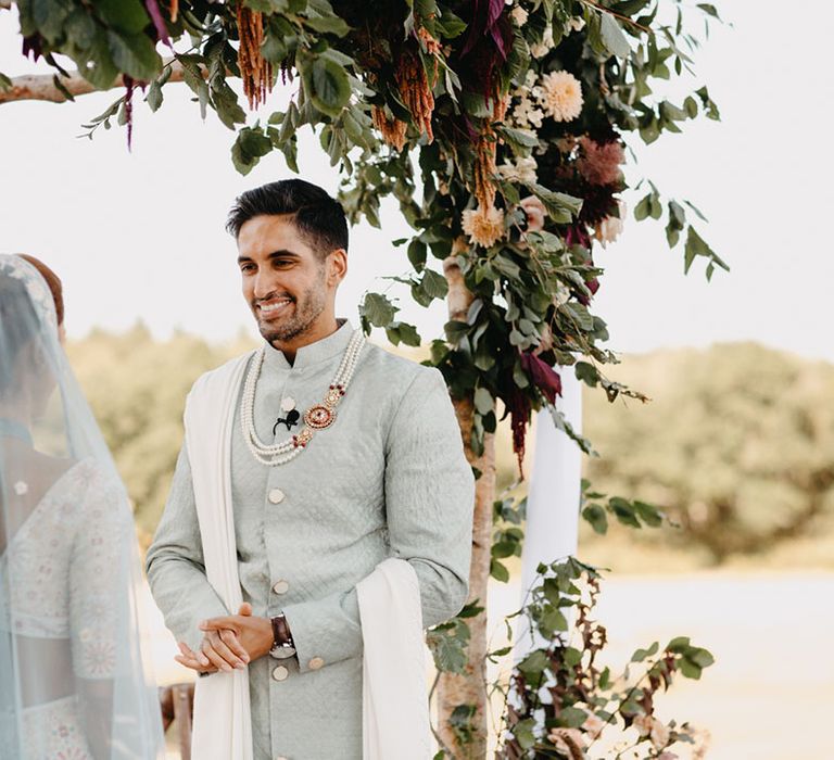 Groom wears pastel sherwani during Indian wedding ceremony outdoors surrounded by florals