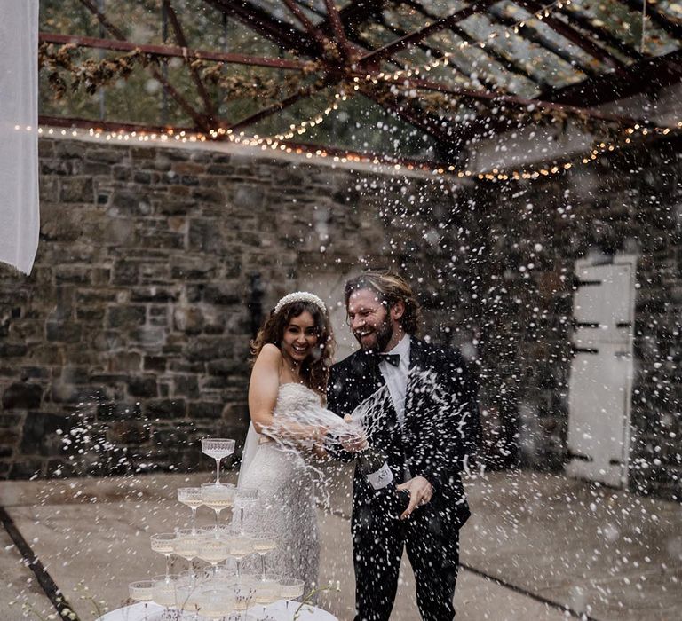 Bride and groom doing champagne pop photo next to champagne tower 