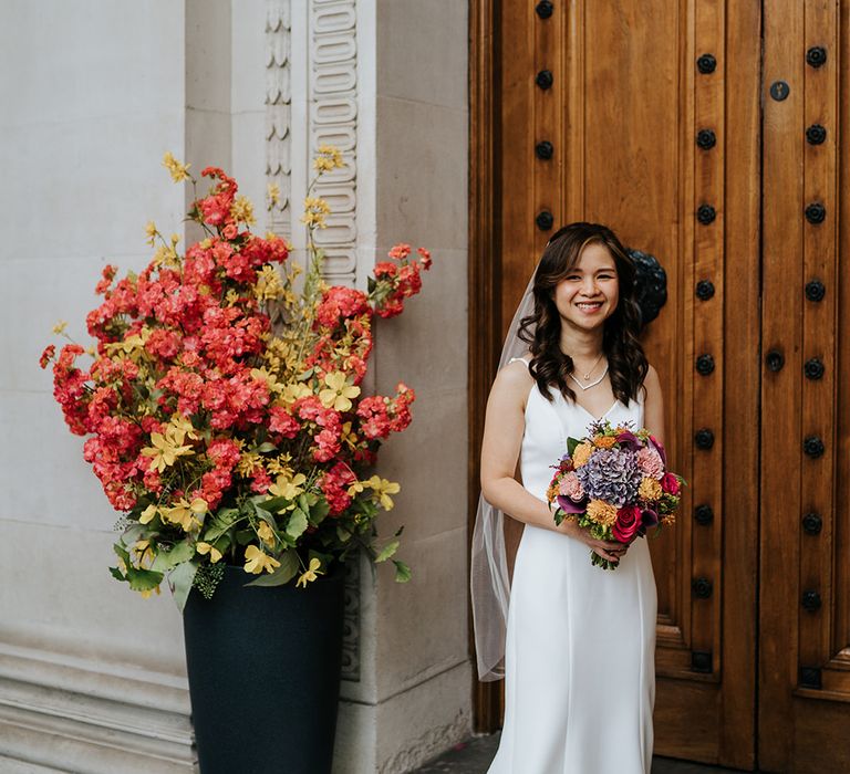 Bride wears her hair in loose curls whilst holding brightly coloured bridal bouquet 