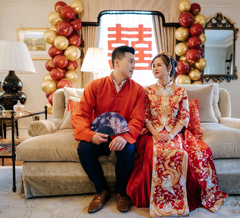 Groom holds colourful fan as he sits beside his bride on their wedding day