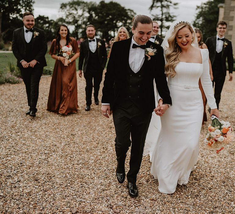 Black tie wedding with bride in long sleeve wedding dress and bridal party and groomsmen walking the grounds of St Tewdrick's wedding venue in Wales