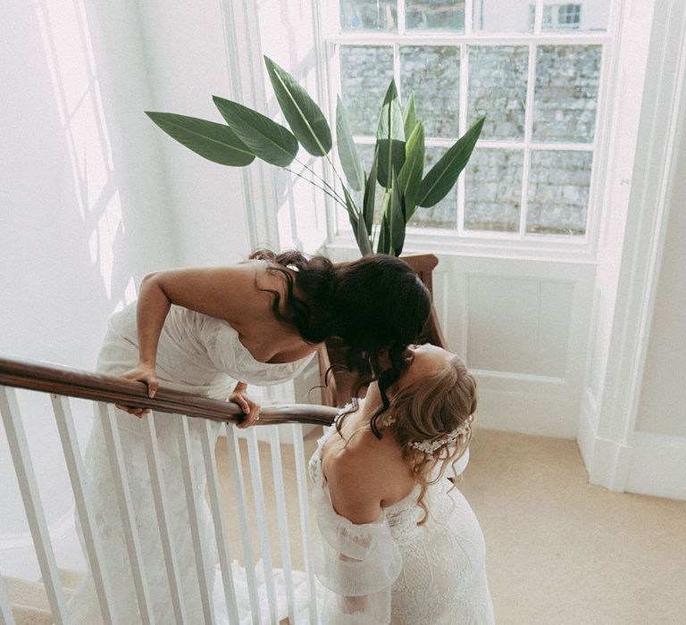 Brides in off the shoulder long sleeve wedding dress and strapless lace wedding dress kissing on the stairs