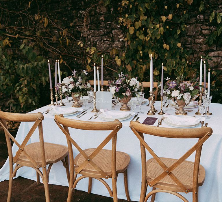 Intimate and neutral wedding tablescape with lavender and white tapered candles in gold candle holders, lavender wedding menus and mixed floral arrangements with white carnations, purple tulips, roses and foliage