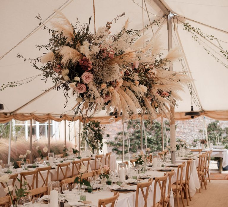 Marquee wedding reception with large flower installation with pampas grass and pink flowers over a green and white tablescape 