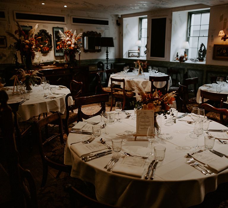 Circular wedding table at The Zetter Townhouse with white table cloth, large autumnal floral arrangement in clear vase 