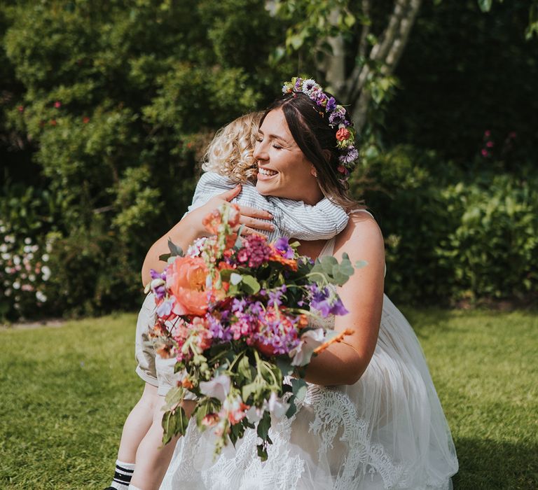 Bride holding colourful floral bouquet hugs her son outdoors