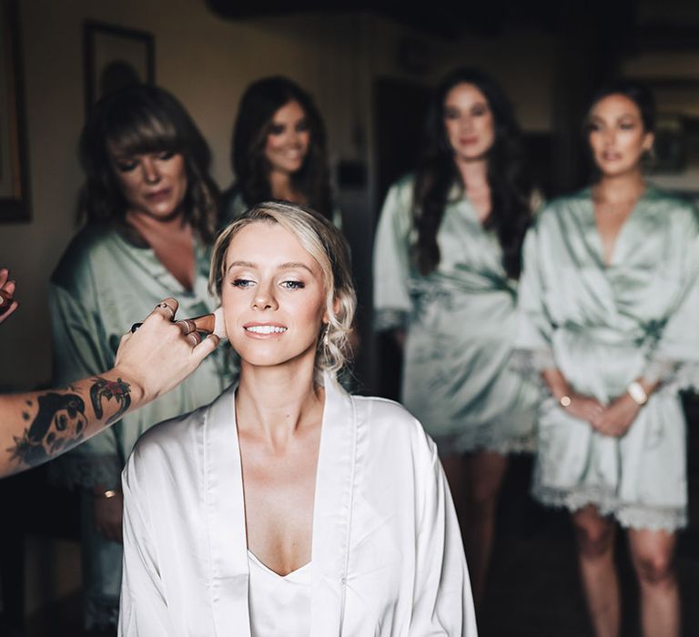 Blonde bride in silk white pyjamas has her makeup done and bridesmaids in silk pale green pyjamas watch on 