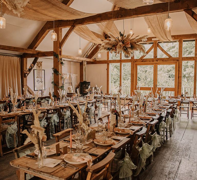 Sage green sheer ribbon chair back decor with a pampas grass flower installation, disco balls and drapes for rustic barn wedding 