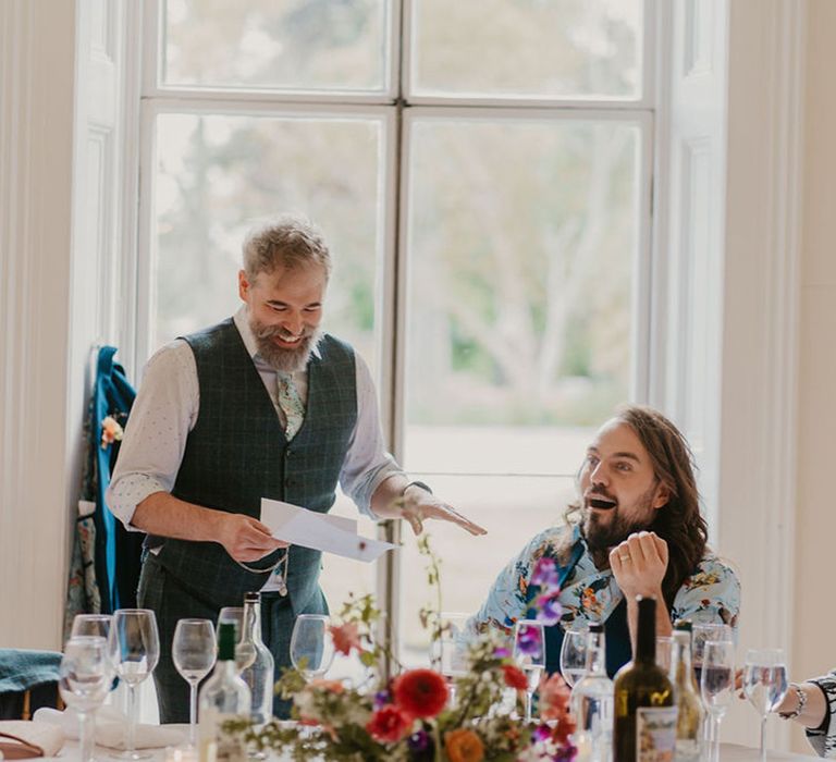 Groom in tartan waistcoat and white shirt reads speech during intimate reception 