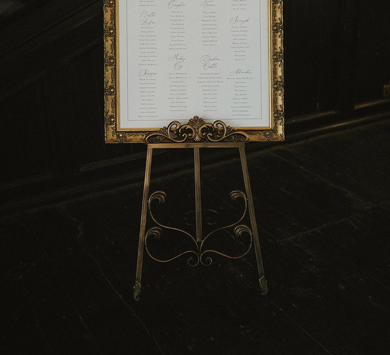 Black and white wedding table plan and seating chart with gold frame on easel 