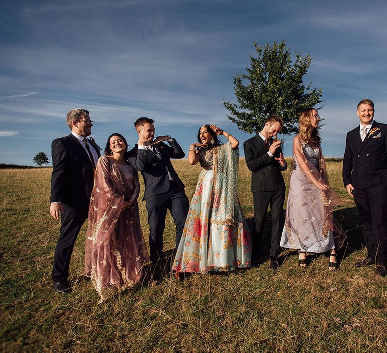 Bride & groom stand with their groomsmen in suits and bridesmaids in pink long sleeve satin bridesmaid dresses 