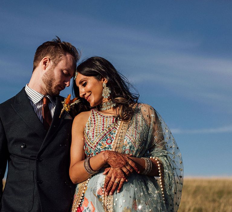 Bride wearing colourful lenenga leans in to her groom during golden hour outdoor portraits 