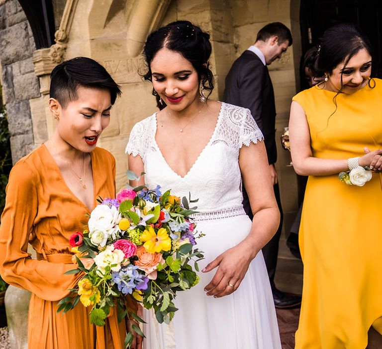 Bridesmaid wears orange wrap dress and holds colourful floral bouquet 