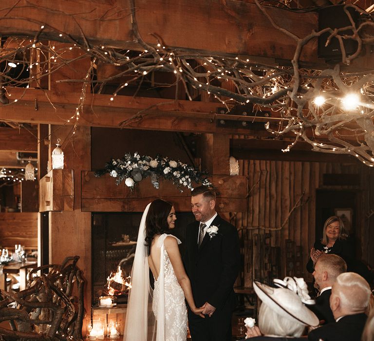 Cosy and rustic Alnwick Treehouse wedding with the bride in a lace wedding dress holding hands with the groom as the guests clap for them