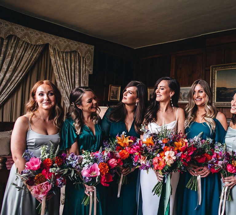 Bridesmaids in light and dark green mismatched bridesmaid dresses with the bride in a satin gown holding bright wedding bouquets 