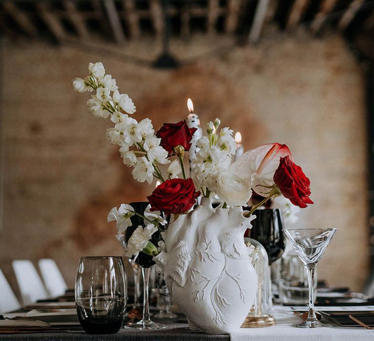 White anatomic heart vase with white carnations, red roses and white peonies on contemporary monochrome wedding tablescape at Woolwich Works London wedding venue 