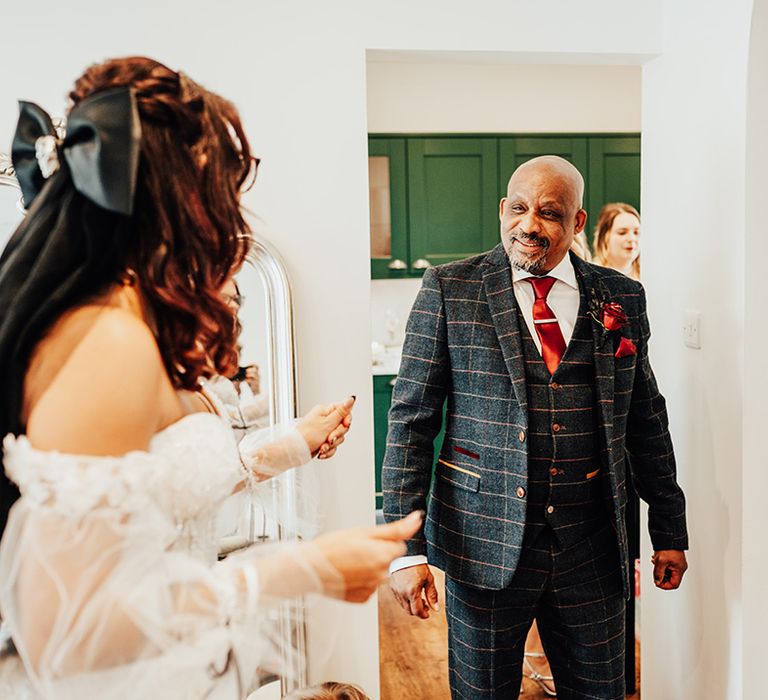 Father of the bride in navy blue suit with orange checkered pattern sees the bride for the first time in a off the shoulder wedding dress with embellishments 