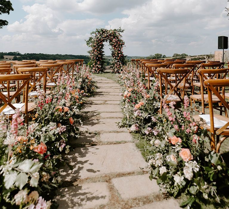 An outdoor wedding at Botley Hill Barn wedding venue with big floral arch and with pink and orange flower aisle decorations 