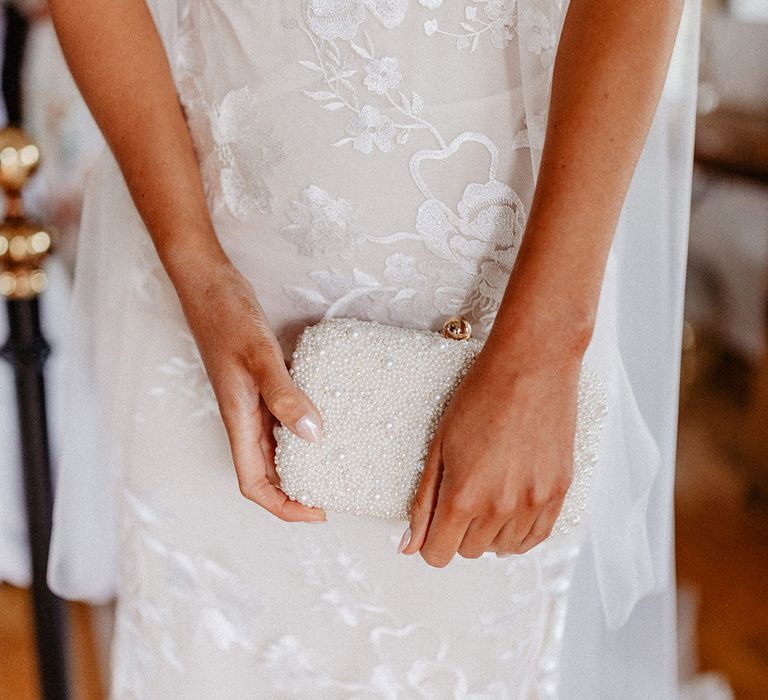 Bride in lace wedding dress with chrome wedding nails holding a pearl bridal clutch 