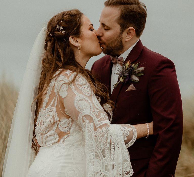 Boho wedding with the bride in a bell sleeve wedding dress and the groom in a three piece burgundy suit posing for their couple portraits 