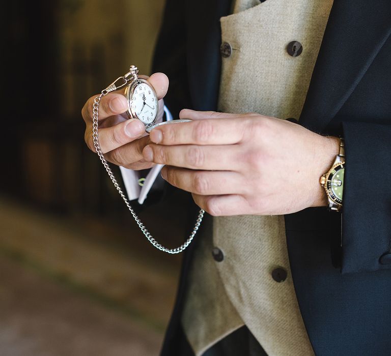 Groom in navy suit with beige waistcoat holding silver pocket watch groom accessory for the wedding