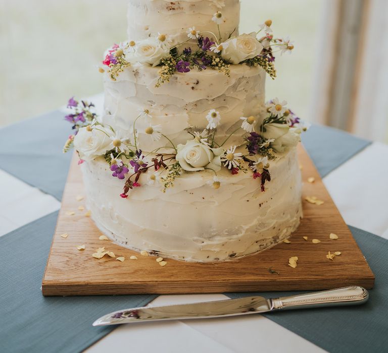 Three tier rustic white iced wedding cake with daisies and roses 