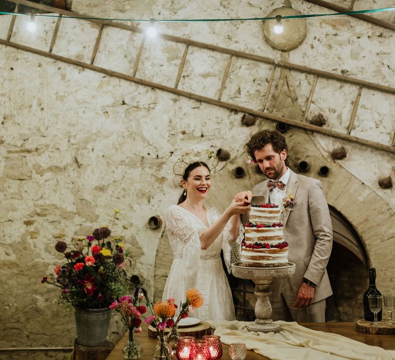 Bride and groom at rustic weddng venue in italy cutting a naked wedding cake covered in mixed berries