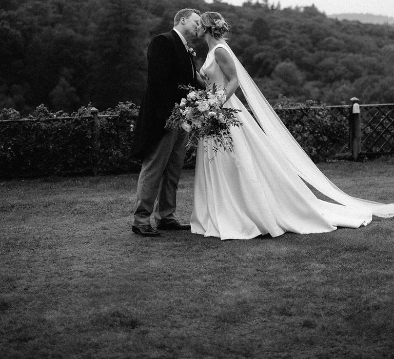 Groom in morning suit kisses the bride in a San Patrick wedding dress with wedding veil