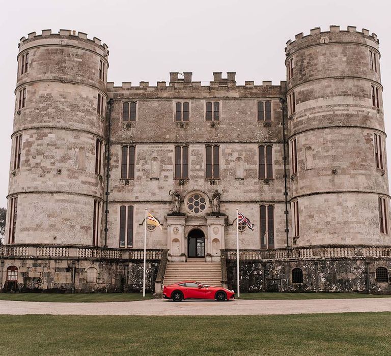 Lulworth Castle wedding venue in Dorset with the bride's red Ferrari wedding car parked outside 