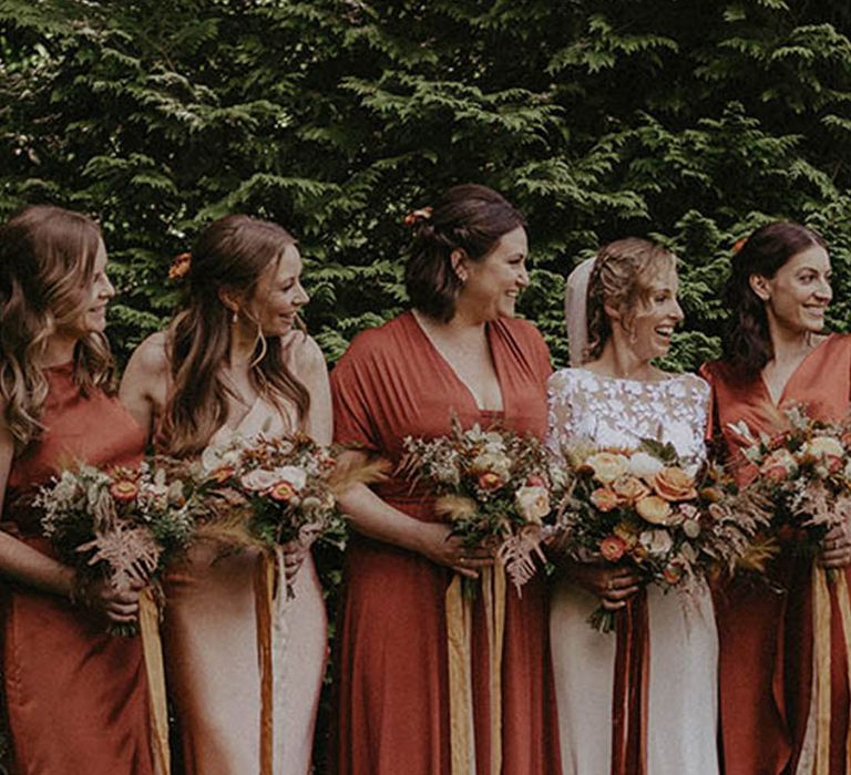 Bride in lace wedding dress with bridesmaids in mismatched orange dresses with some wearing midi styles, satin styles and more 