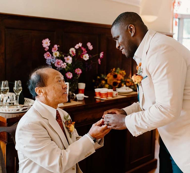 Groom in cream grooms morning suit partaking in Chinese Tea Ceremony wedding tradition at Broadfield Court