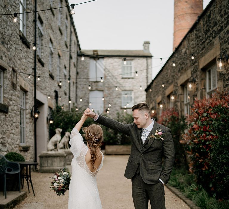 Groom in three piece navy wedding suit spins the bride in a dotted wedding dress around on her wedding day 