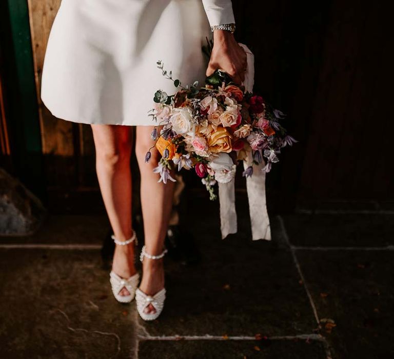 Bride in long sleeve short wedding dress and platform pearl wedding heels holding mixed bridal bouquet with garden roses, carnations, peonies and foliage 