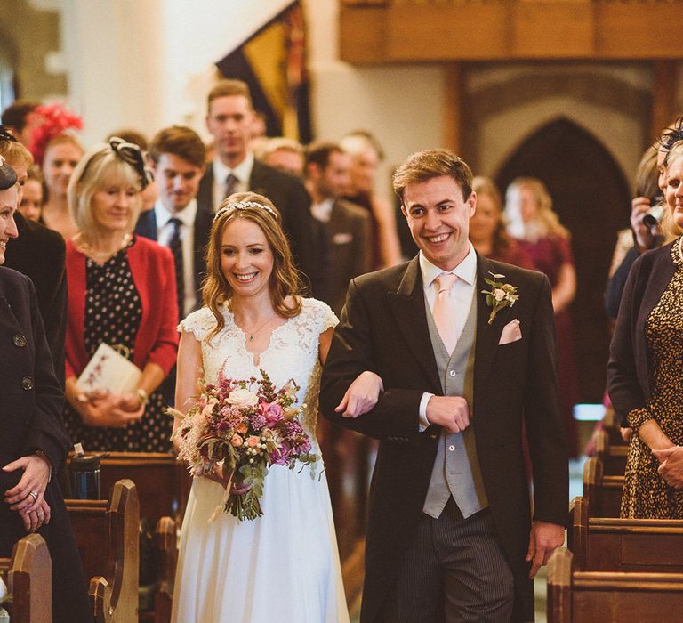 Bride in lace cap sleeve wedding dress with diamante hairpiece walking down the aisle 