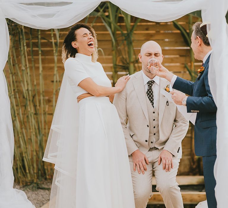 Bride laughing at groom drinking at traditional Jewish wedding ceremony 