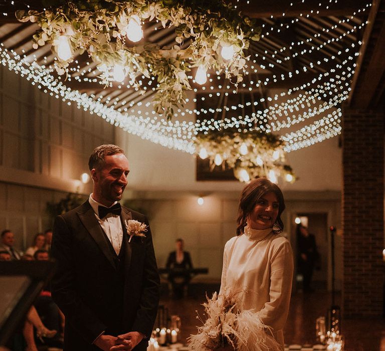 Bride in high neck long sleeve short wedding dress with feathers with groom in black tie at Larkspur Lodge wedding 