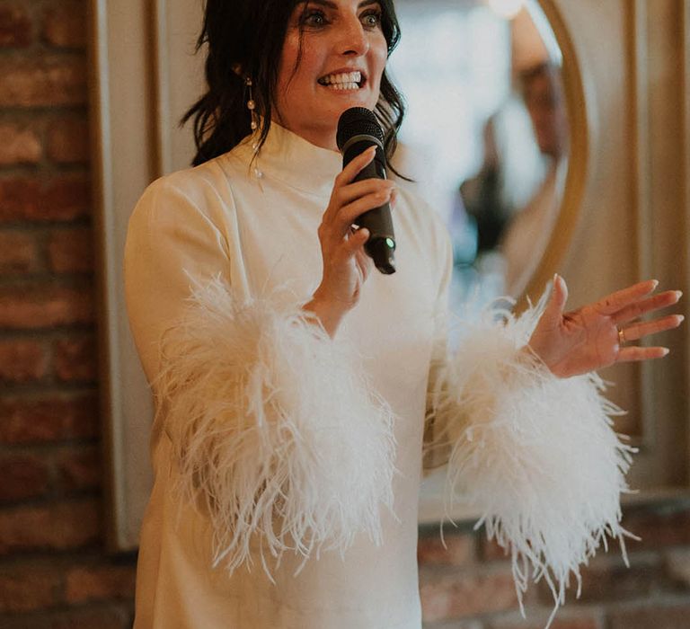 Bride in long sleeve short leather wedding dress with dangling Cult Gaia earrings reading her wedding speech 