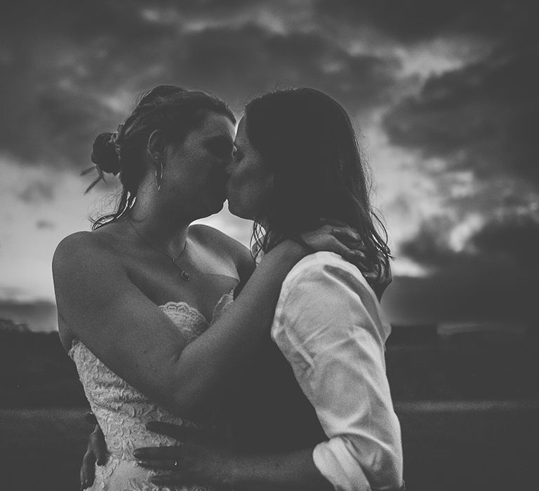 black and white atmospheric photo of two brides kissing in a field 