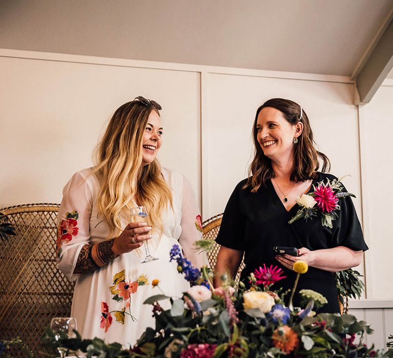 Bride in colourful embroidered floral wedding dress with bride in black jumpsuit standing at their sweetheart table 