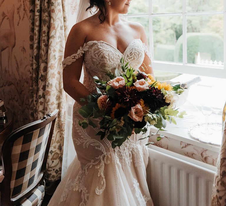 Bride wearing off the shoulder sweetheart lace wedding dress with veil holding bouquet with sunflowers 