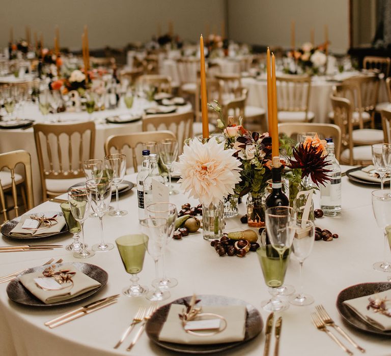 Round tables decorated with orange taper candles with neutral centrepieces and flowers 