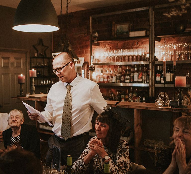 Father of the groom reads out wedding speech at spooky wedding with gothic and autumnal styling 