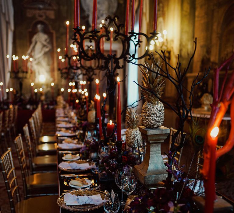 Red, black and gold gothic wedding table decorations with dark purple flowers, sprayed gold pineapple exotic fruits 