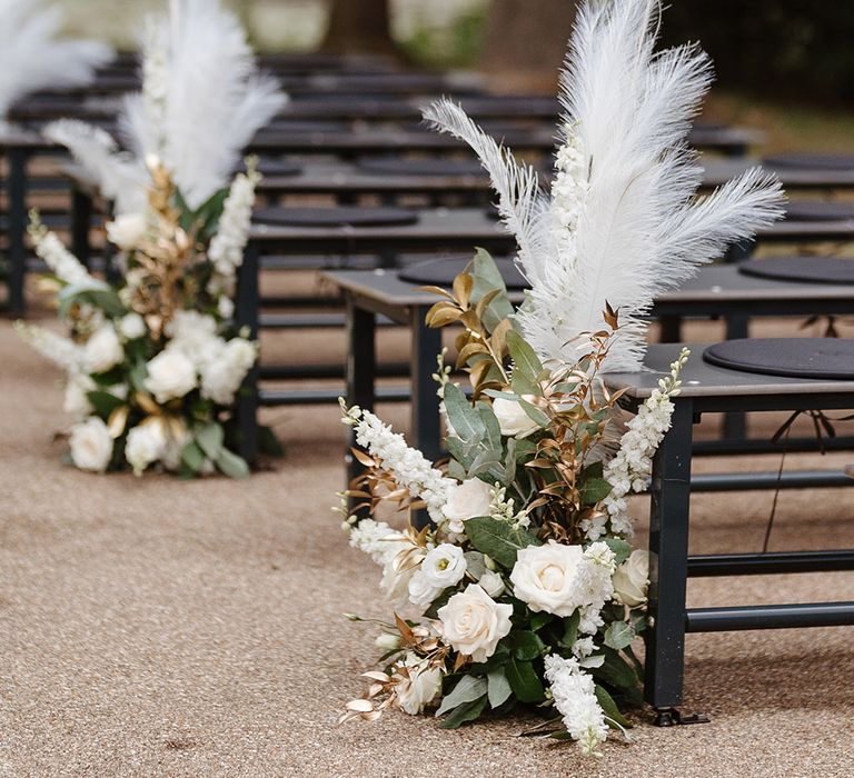 Outdoor wedding ceremony with black benches with white floral aisle decorations with pampas grass 