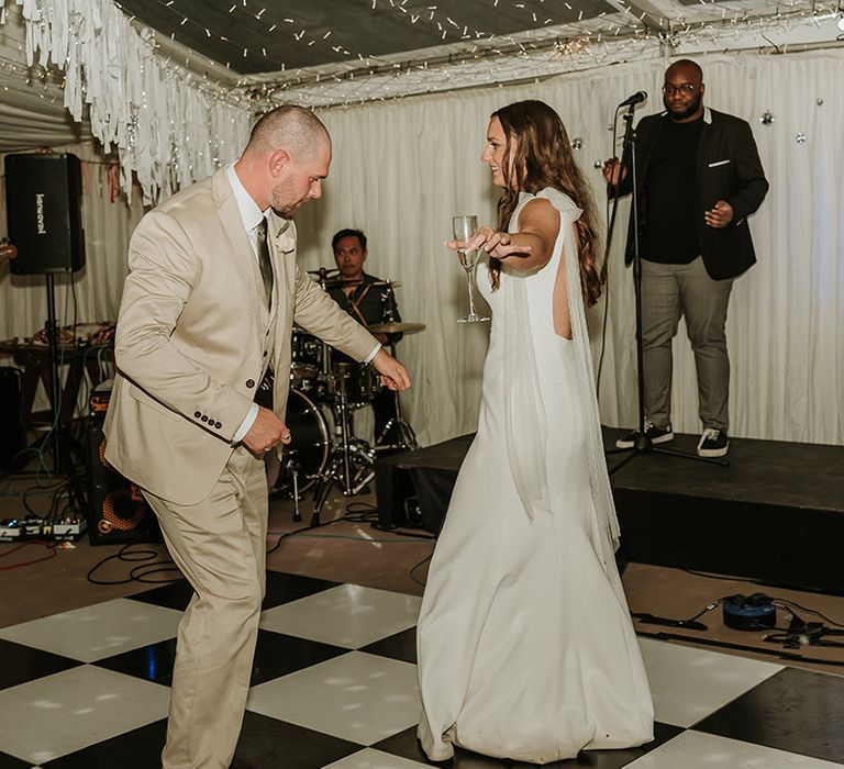 The bride and groom have their first dance together on black and white checkered dance floor at home marquee wedding 