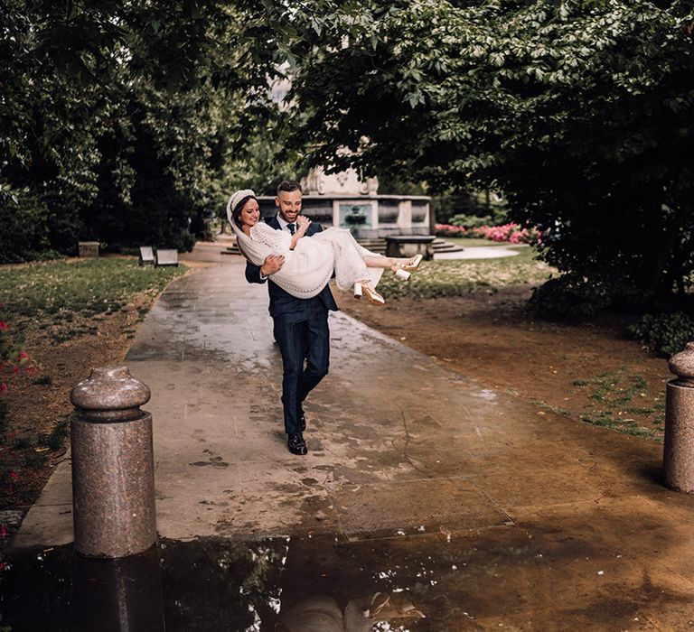 The groom carries the bride over a puddle on rainy wedding day 