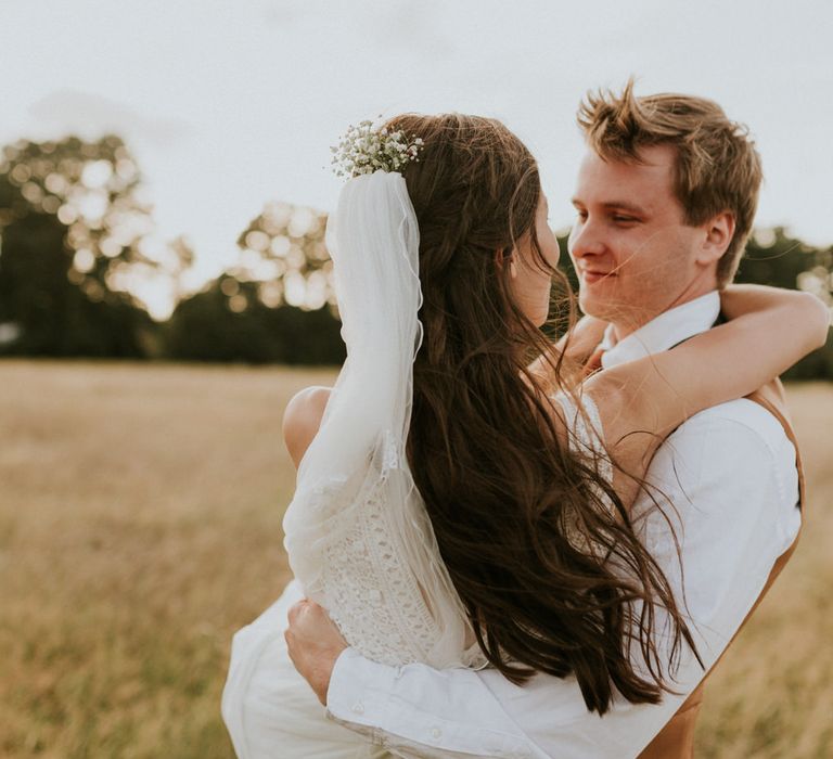 Portrait of the groom picking his bride up in a field 