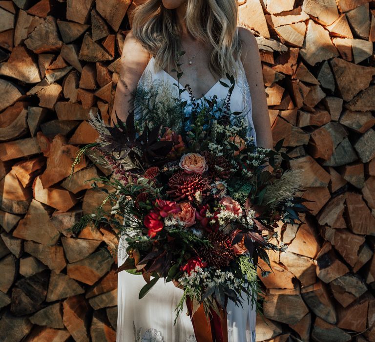 Blonde bride holding Autumnal bouquet in front of logs