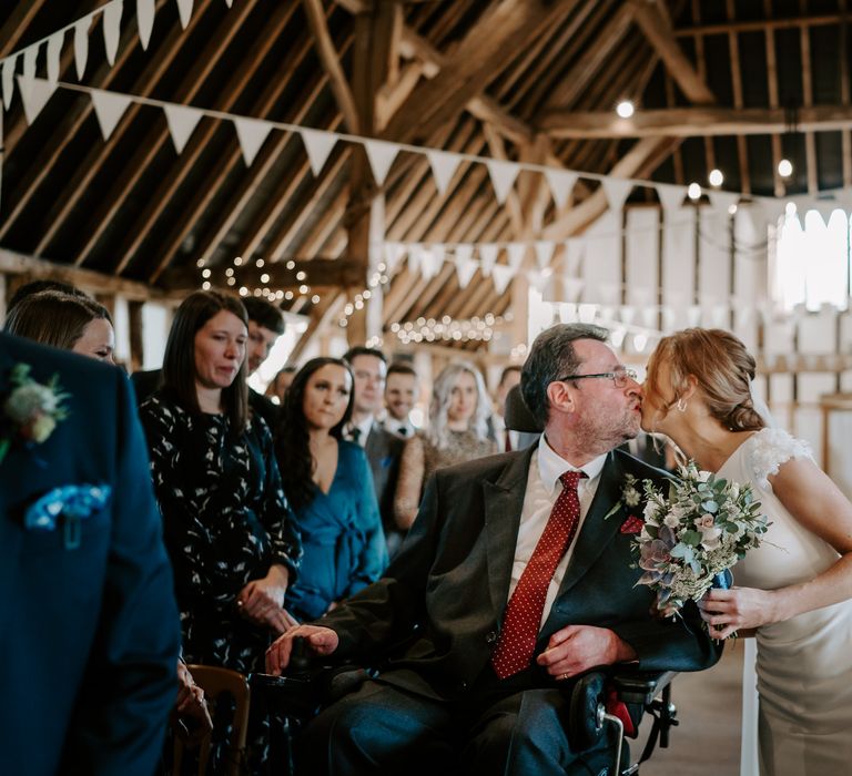 Bride in a fitted Pronovias wedding dress holding a succulent wedding bouquet kissing her father at the bottom of the aisle 