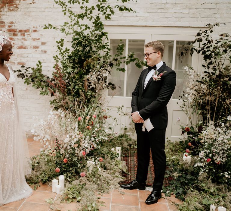 Bride and groom first look with the bride in an embellished wedding dress with cape and the groom in a black tie suit and bow tie. 